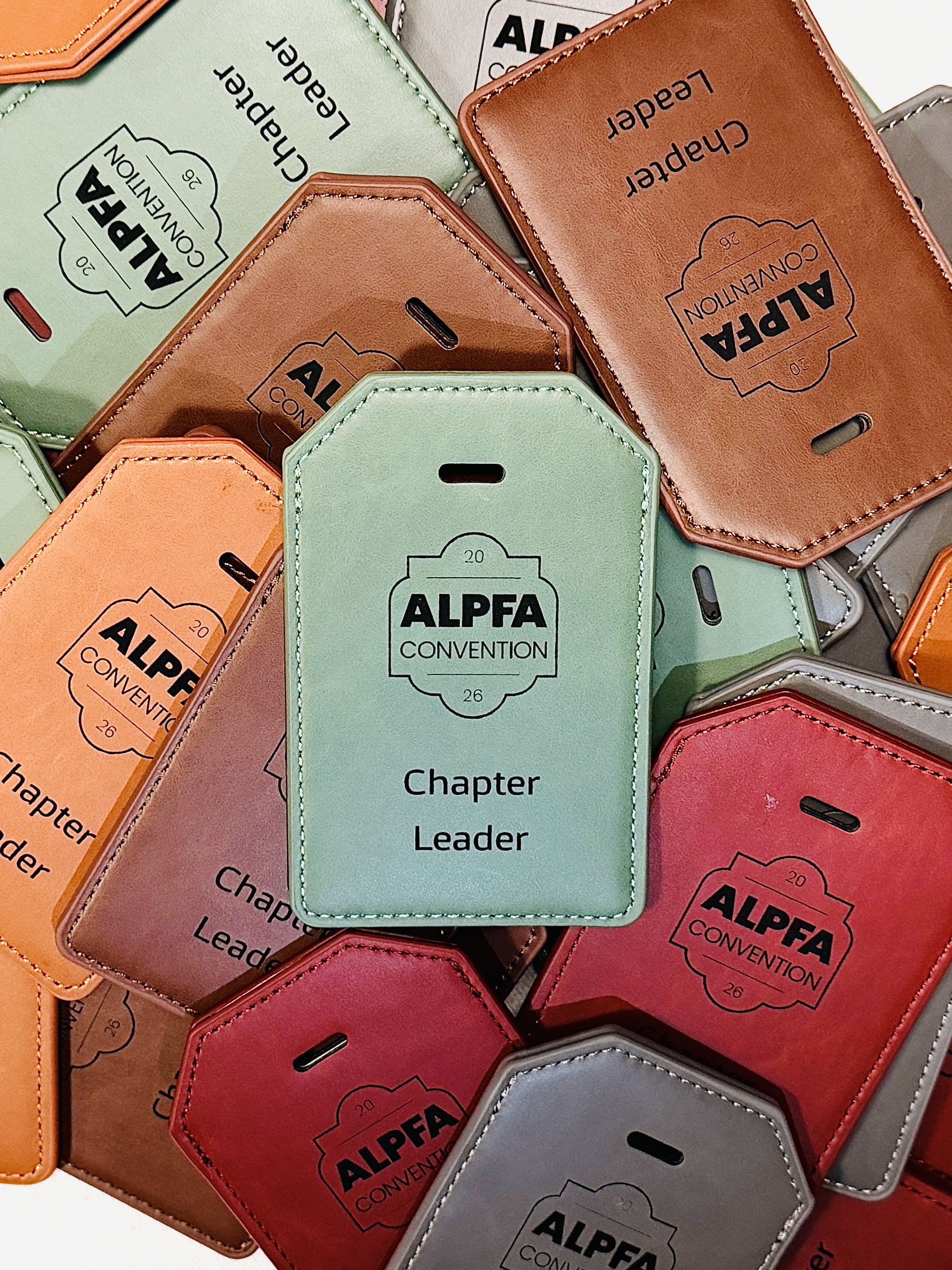 Engraved leatherette luggage tags in five colors, laid out after a bulk order.